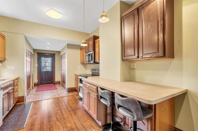 kitchen with brown cabinets, hanging light fixtures, baseboards, light wood-style flooring, and appliances with stainless steel finishes