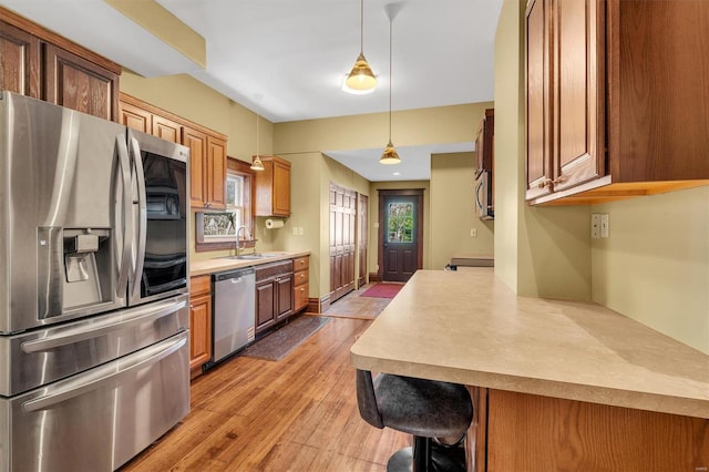 kitchen with a sink, brown cabinetry, light wood-type flooring, stainless steel appliances, and light countertops