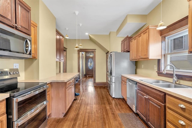 kitchen featuring a sink, pendant lighting, light countertops, dark wood finished floors, and appliances with stainless steel finishes