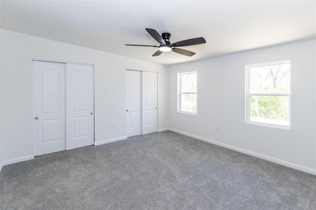 unfurnished bedroom with carpet, multiple closets, baseboards, and ceiling fan