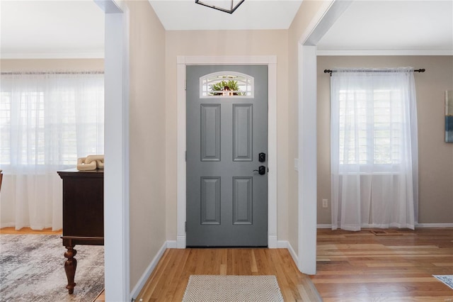 entrance foyer featuring light wood-type flooring, ornamental molding, baseboards, and plenty of natural light