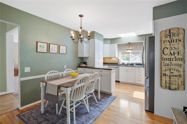 dining area with a skylight, baseboards, light wood-style flooring, and a notable chandelier