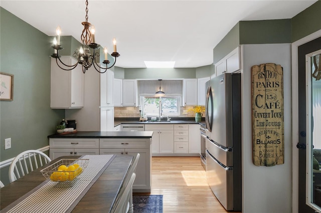 kitchen with dark countertops, a notable chandelier, light wood-style floors, stainless steel appliances, and tasteful backsplash