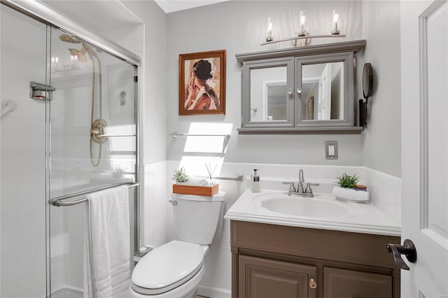bathroom with tile walls, wainscoting, a shower stall, vanity, and toilet