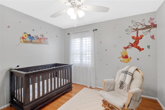 bedroom featuring light wood-type flooring, a ceiling fan, a crib, and baseboards