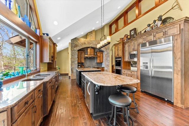 kitchen featuring dark wood-style flooring, a sink, built in appliances, decorative backsplash, and a kitchen island