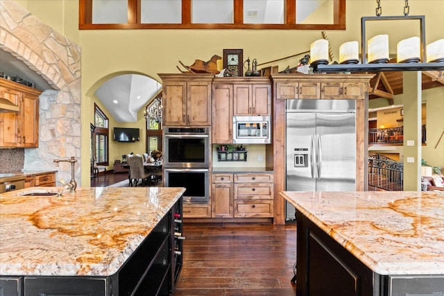 kitchen with dark wood-style flooring, arched walkways, light stone countertops, a sink, and built in appliances