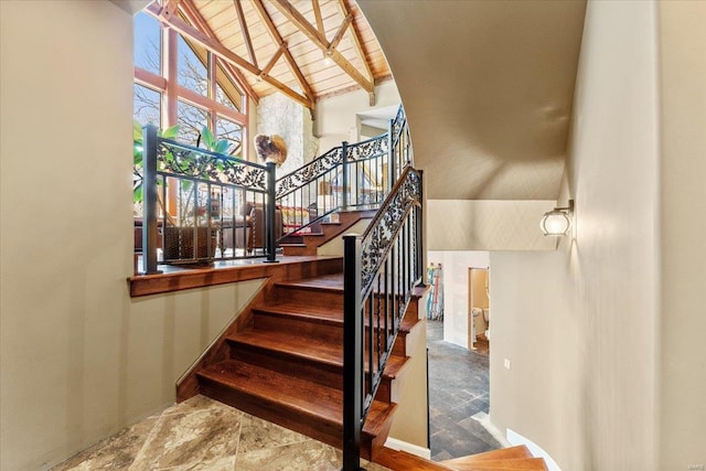 stairway with baseboards, beam ceiling, stone finish floor, and high vaulted ceiling