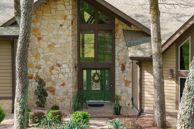 entrance to property featuring a shingled roof and stone siding