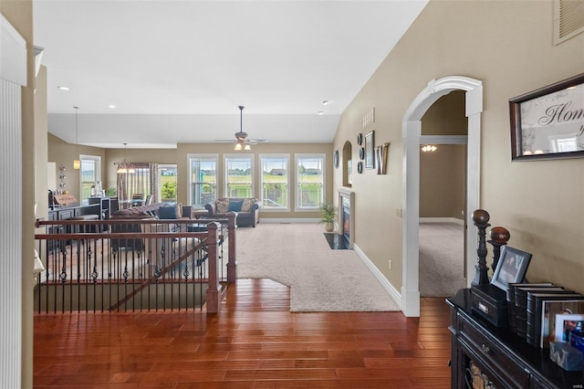 corridor with wood finished floors, arched walkways, carpet, baseboards, and visible vents