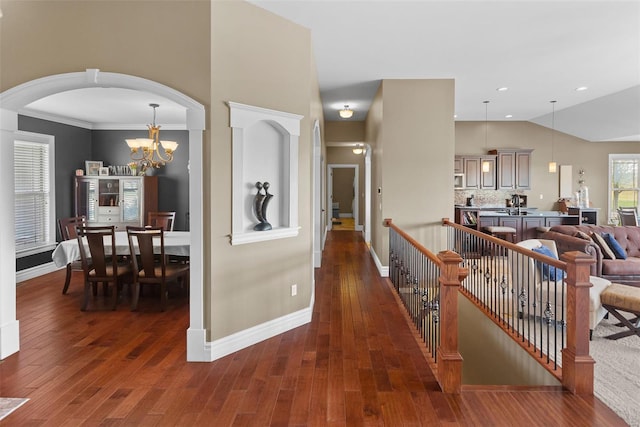 corridor featuring baseboards, wood finished floors, arched walkways, and a chandelier