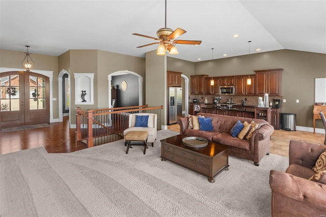 living area featuring lofted ceiling, a ceiling fan, french doors, arched walkways, and baseboards