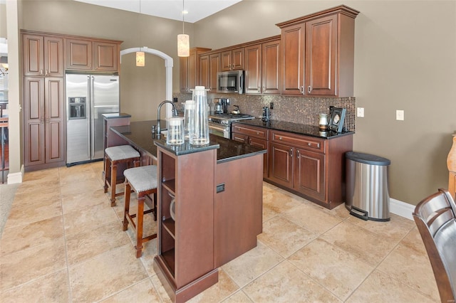 kitchen with a kitchen island with sink, arched walkways, tasteful backsplash, a kitchen bar, and high quality appliances