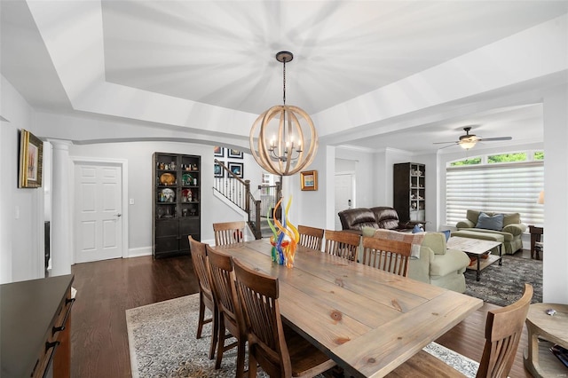 dining space with dark wood-style flooring, stairway, a raised ceiling, baseboards, and ceiling fan with notable chandelier