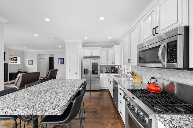 kitchen with crown molding, appliances with stainless steel finishes, light stone countertops, a sink, and recessed lighting