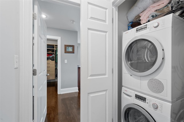 clothes washing area featuring baseboards, stacked washer and clothes dryer, dark wood-style flooring, and laundry area
