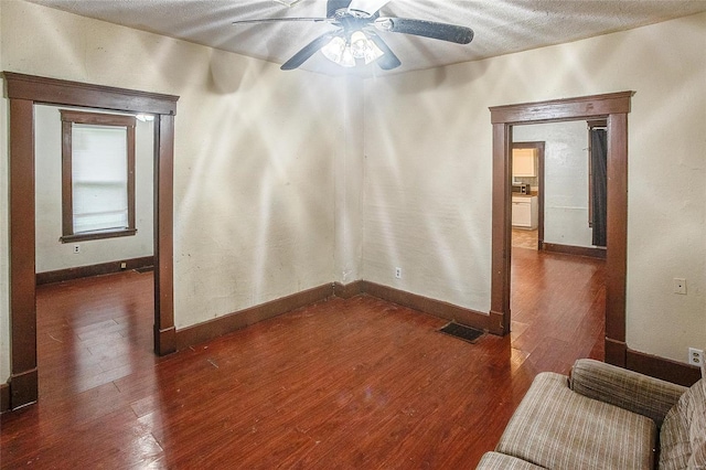 interior space with baseboards, a ceiling fan, visible vents, and dark wood-style floors