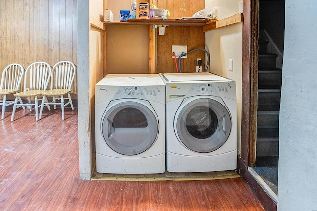 clothes washing area with independent washer and dryer, wood finished floors, wood walls, and laundry area