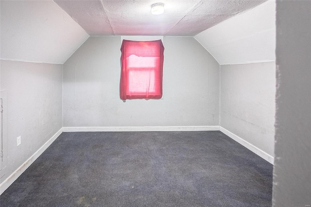 additional living space with vaulted ceiling, dark colored carpet, and baseboards
