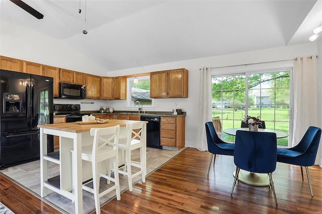 kitchen with brown cabinetry, black appliances, lofted ceiling, light wood-style floors, and wood counters