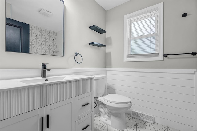bathroom with visible vents, toilet, vanity, and wainscoting