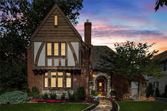 tudor home featuring brick siding, a chimney, a front yard, and stucco siding