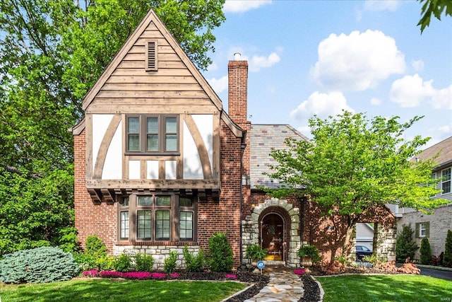 tudor home featuring brick siding, a front lawn, and a chimney