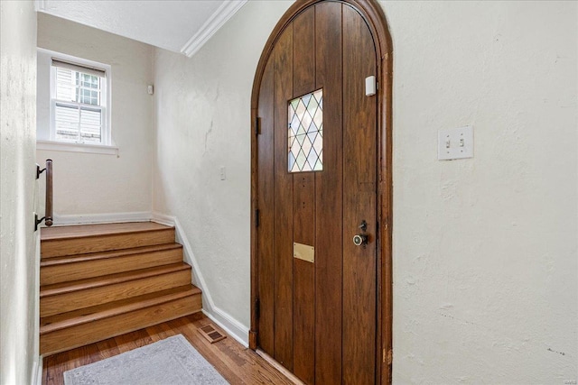 entrance foyer featuring visible vents, ornamental molding, wood finished floors, baseboards, and arched walkways