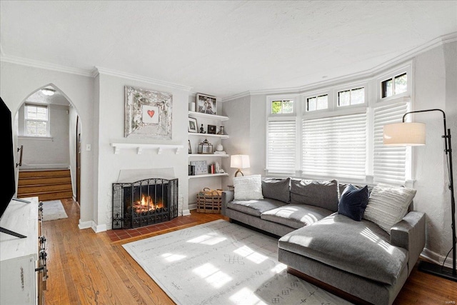 living room featuring arched walkways, a fireplace with flush hearth, ornamental molding, and wood finished floors