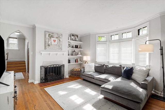 living room with crown molding, arched walkways, a fireplace with flush hearth, baseboards, and hardwood / wood-style floors