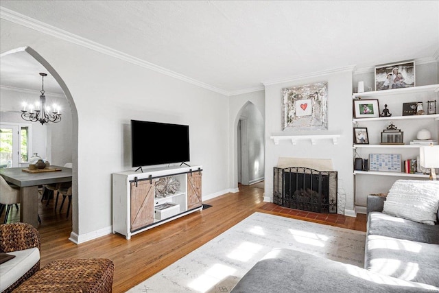 living area featuring a fireplace with flush hearth, arched walkways, wood finished floors, a notable chandelier, and ornamental molding