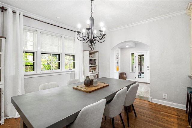 dining area with crown molding, arched walkways, an inviting chandelier, and dark wood finished floors