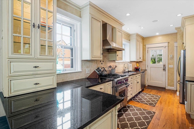 kitchen with a sink, cream cabinets, stainless steel appliances, and wall chimney exhaust hood