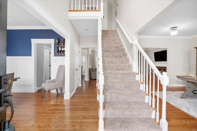 stairway with ornamental molding, a wainscoted wall, a decorative wall, and wood finished floors