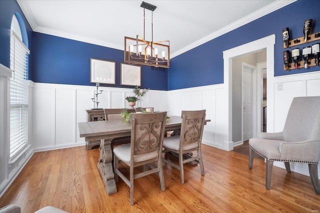 dining space with light wood finished floors, a decorative wall, crown molding, and a chandelier