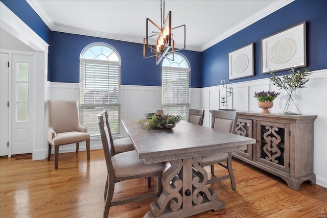 dining area with crown molding, light wood finished floors, an inviting chandelier, and wainscoting