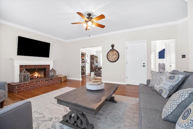 living area featuring crown molding, ceiling fan, baseboards, a brick fireplace, and wood finished floors