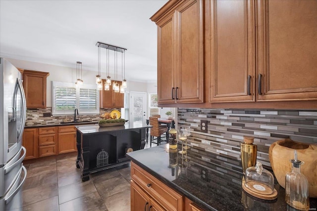 kitchen featuring a sink, decorative backsplash, brown cabinetry, hanging light fixtures, and stainless steel fridge with ice dispenser