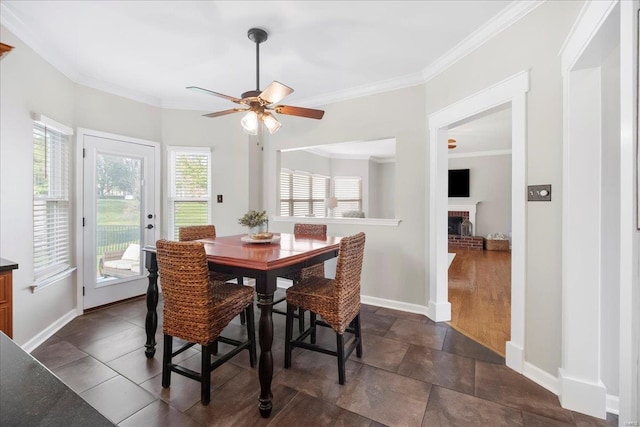 dining space with stone finish floor, a fireplace, baseboards, a ceiling fan, and crown molding