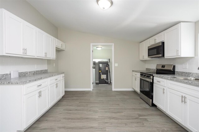 kitchen with a sink, light countertops, stainless steel appliances, baseboards, and lofted ceiling