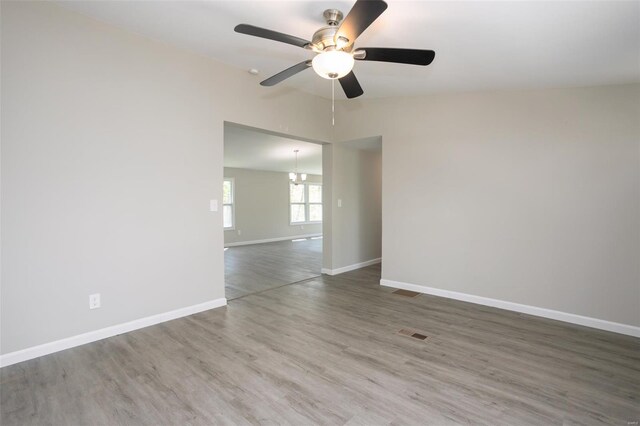 empty room with ceiling fan, visible vents, vaulted ceiling, wood finished floors, and baseboards