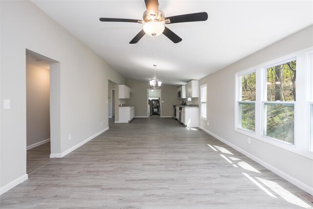 unfurnished living room featuring baseboards, a sink, light wood-style floors, and ceiling fan