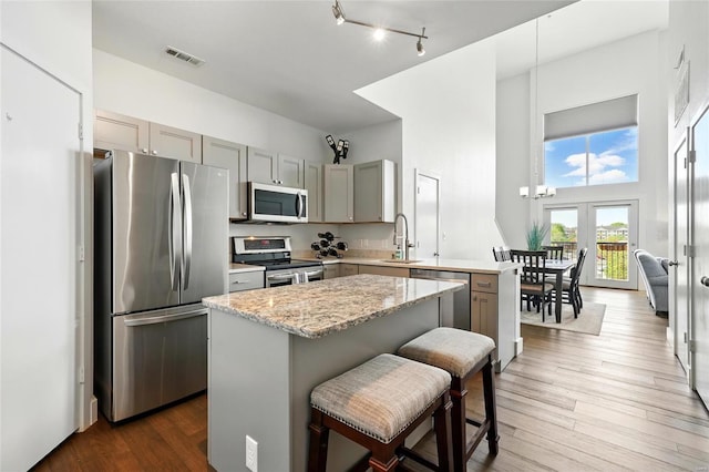 kitchen with stainless steel appliances, a center island, a sink, gray cabinetry, and visible vents