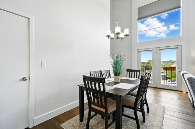 dining space featuring a high ceiling, a chandelier, wood finished floors, baseboards, and french doors
