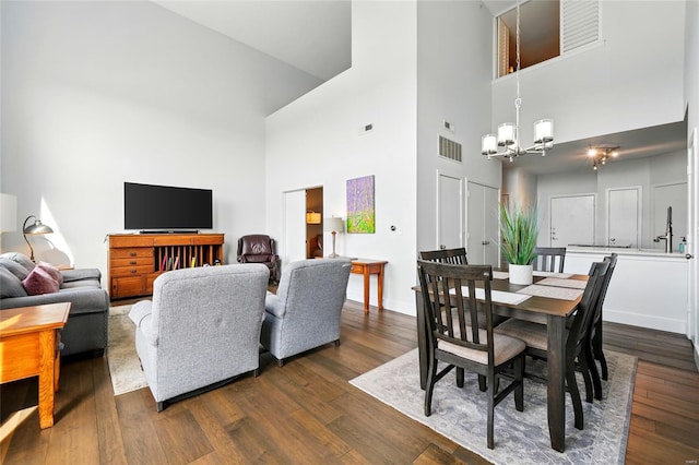 dining area with a high ceiling, a chandelier, dark wood-type flooring, visible vents, and baseboards
