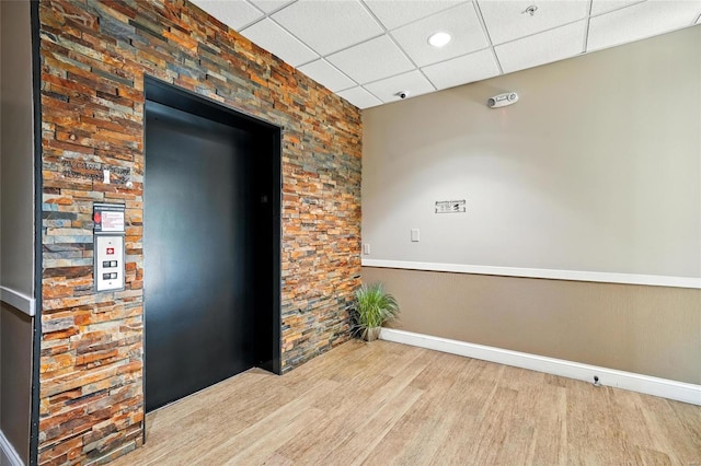 spare room with elevator, wood finished floors, a paneled ceiling, and baseboards