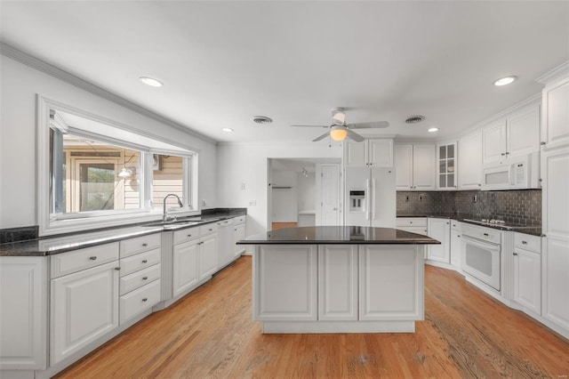 kitchen featuring white cabinetry, dark countertops, white appliances, and a sink