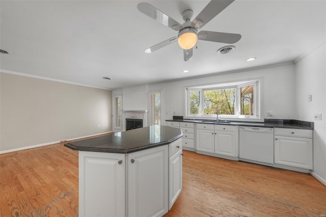 kitchen with a sink, crown molding, dark countertops, dishwasher, and white cabinets