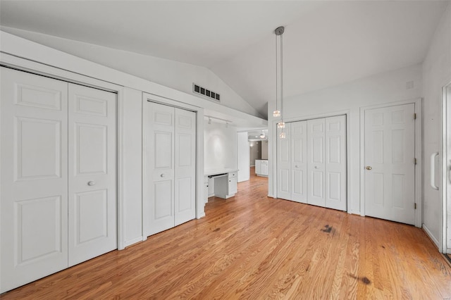 unfurnished bedroom with lofted ceiling, visible vents, multiple closets, and light wood-style floors