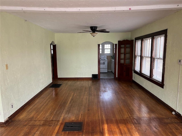 empty room featuring a textured wall, arched walkways, baseboards, visible vents, and hardwood / wood-style flooring